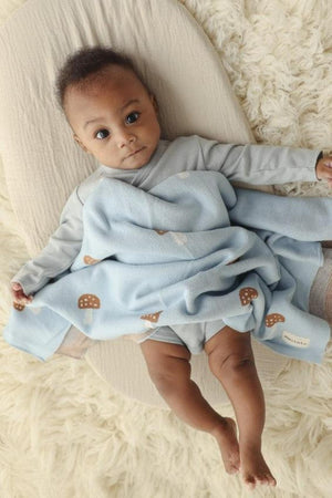 A baby is wrapped in a light blue blanket with mushroom patterns, lying on a soft beige surface.