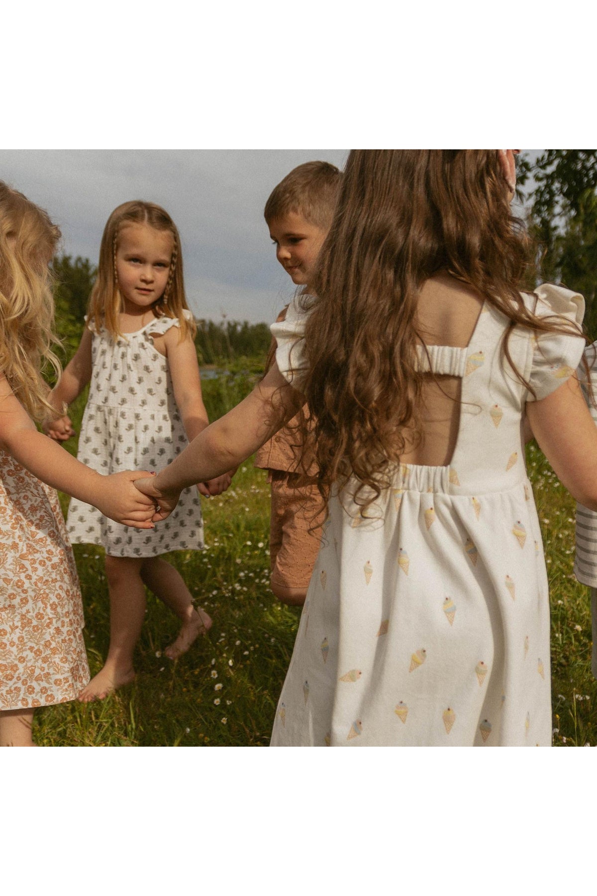 A group of children in a sunny outdoor setting holds hands while wearing playful dresses.