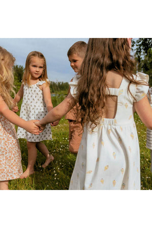A group of children playfully holding hands in a grassy field, wearing various dresses, including a white dress with an ice cream print and a charming cutout back design.