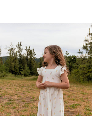A young girl stands in a grassy field, wearing a light-colored dress adorned with an ice cream print.