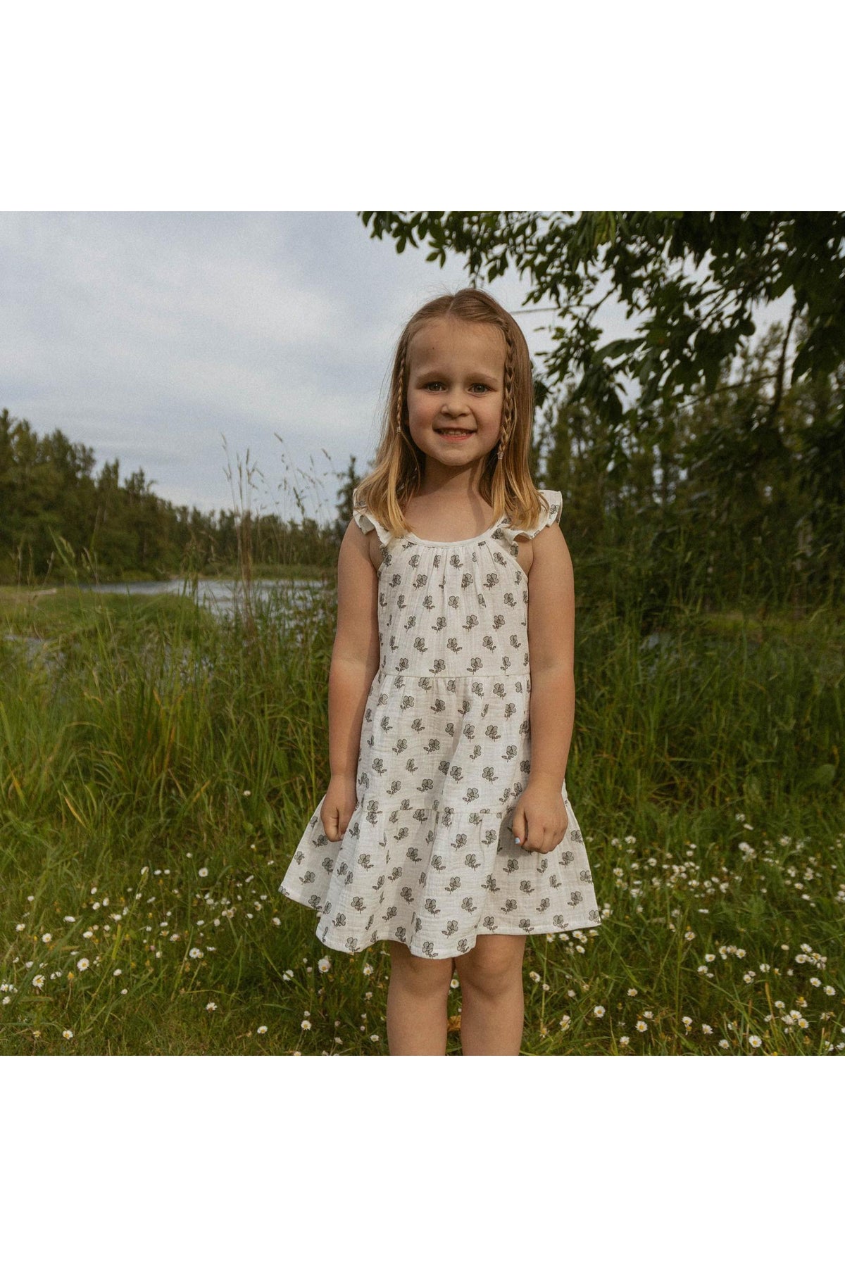 A young girl smiles while wearing a white ruffle tiered dress adorned with a delicate floral pattern.