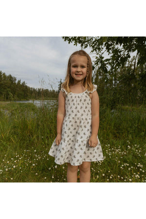 A young girl smiles while wearing a white ruffle tiered dress adorned with a delicate floral pattern.