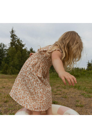 A young child in a flowy, organic cotton sundress with a sienna floral print plays outdoors.
