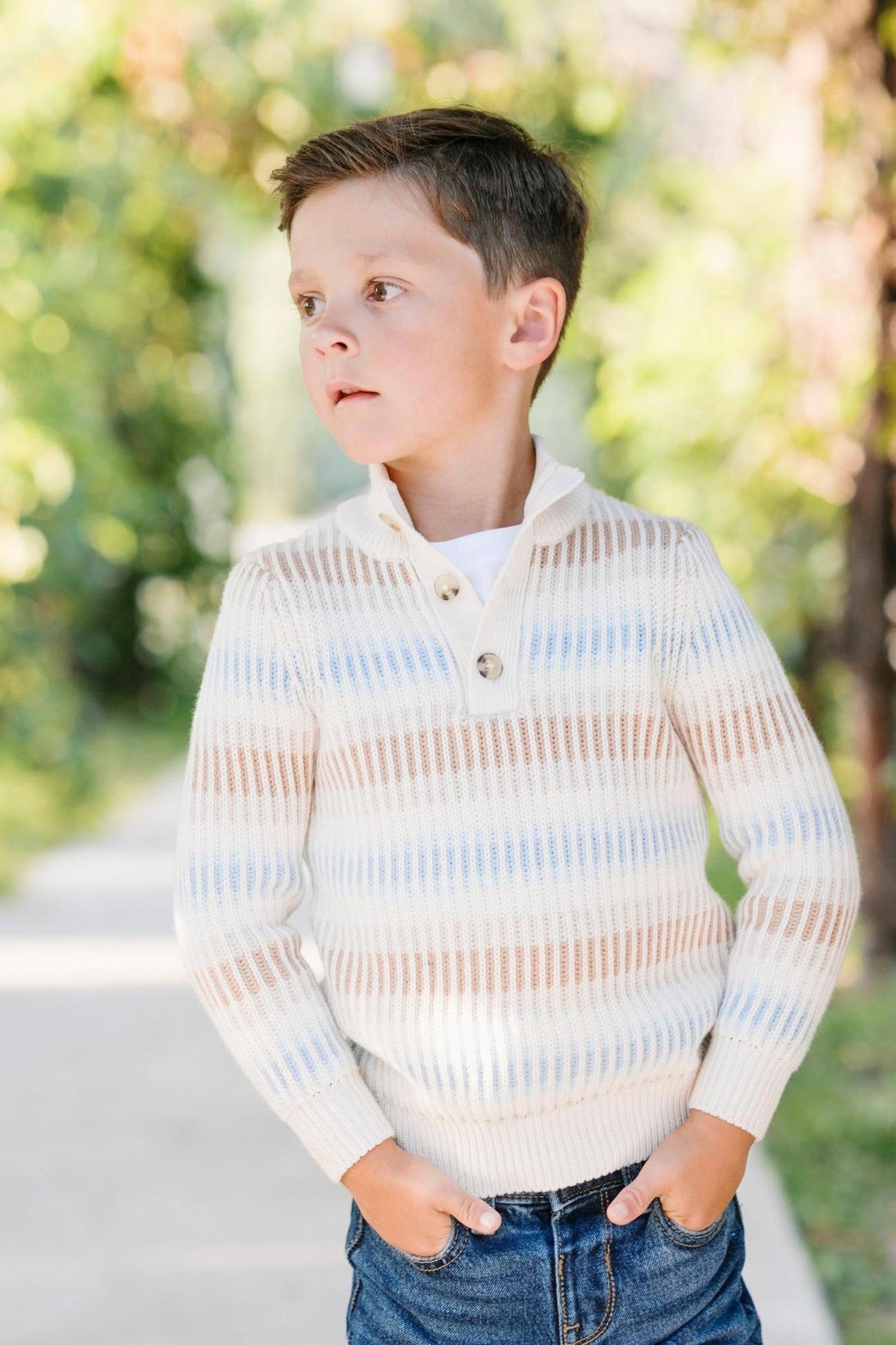 A young boy stands outdoors wearing a cream ombre mock neck sweater with subtle winter stripes.