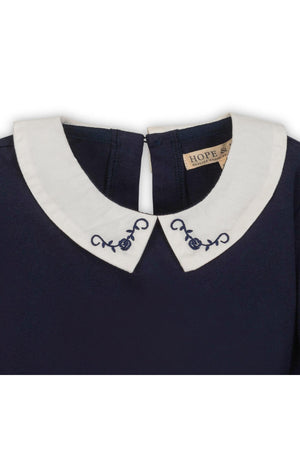 Close-up of a navy knit top featuring a white Peter Pan collar with floral embroidery, designed for girls by Hope.