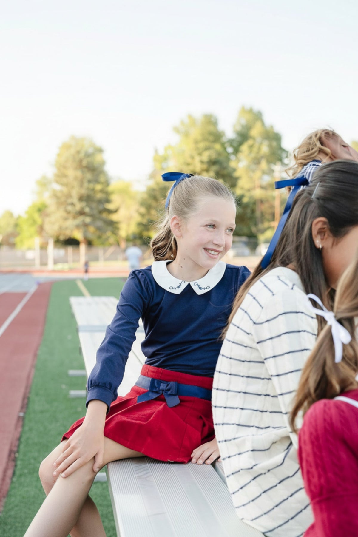 A girl smiles while wearing a navy knit top with a white Peter Pan collar, paired with a red skirt,.