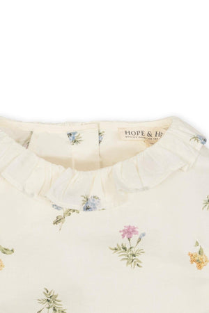 Close-up of an ivory floral top featuring a ruffle collar, made from soft organic cotton with delicate flower prints.
