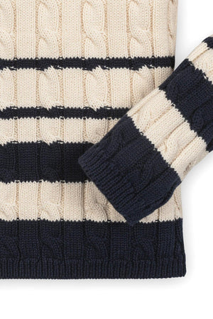 A close-up of a cream and navy striped knitted sweater featuring a cable pattern and ribbed cuffs.
