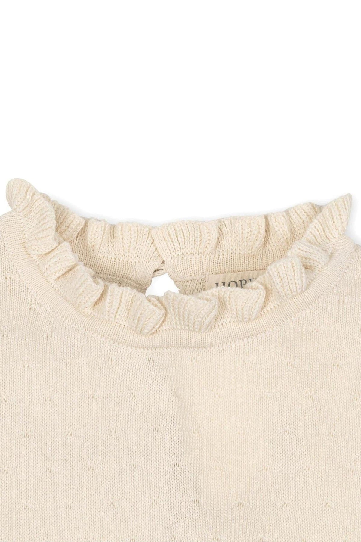 Close-up of an ivory organic cotton sweater featuring a ruffled collar and a back keyhole closure.