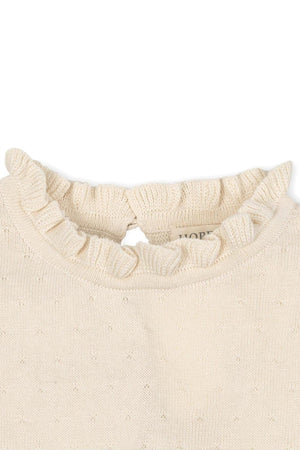 Close-up of an ivory organic cotton sweater featuring a ruffled collar and a back keyhole closure.