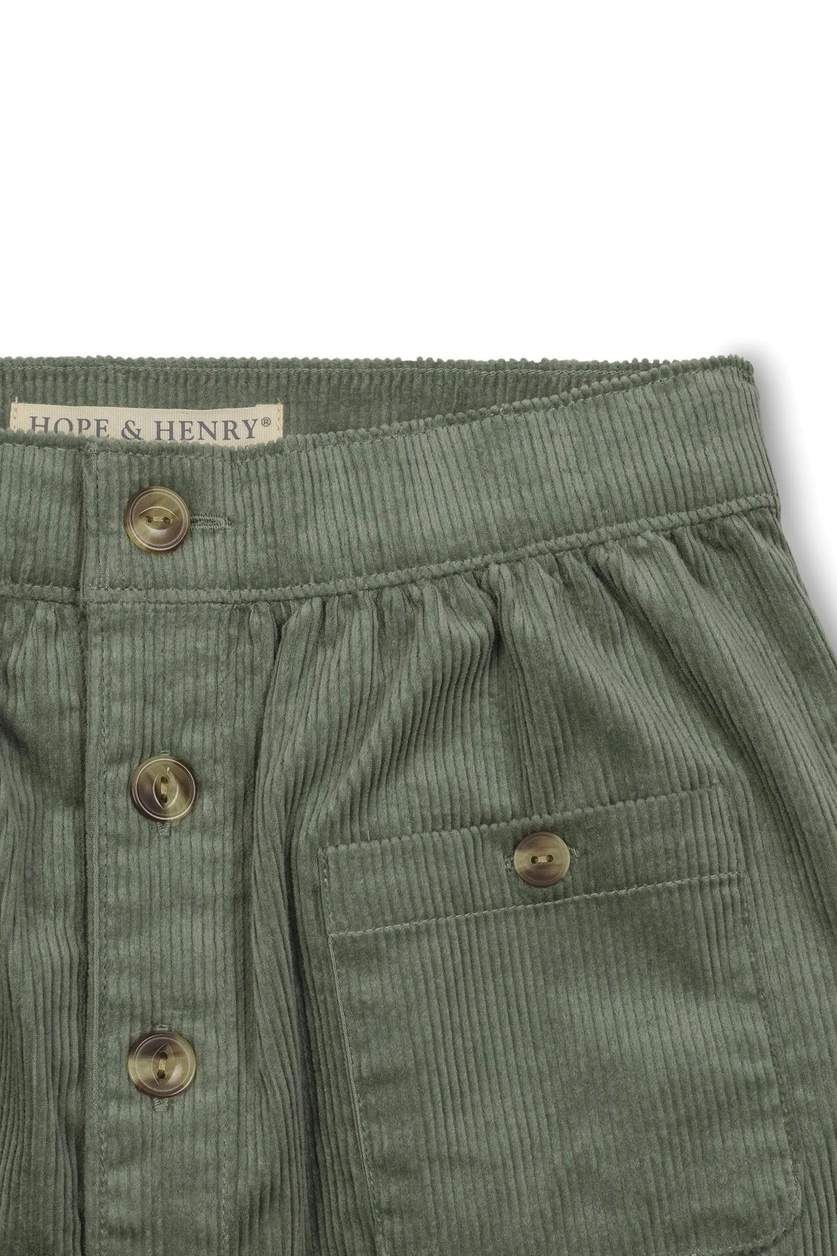Close-up of a sage green corduroy skirt featuring faux horn buttons, a gathered waistband, and a patch pocket.