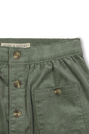 Close-up of a sage green corduroy skirt featuring faux horn buttons, a gathered waistband, and a patch pocket.