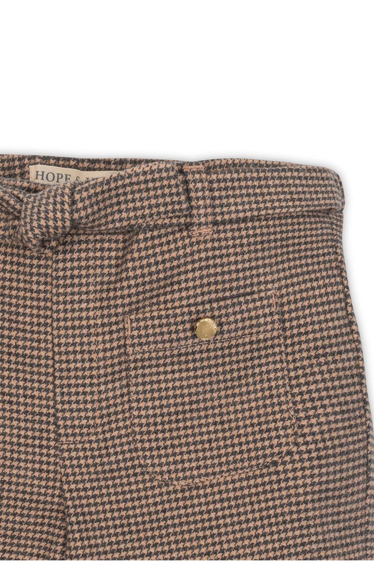 Close-up of camel houndstooth wide-leg pants featuring a faux waist tie and a gold button detail. Made from organic cotton.
