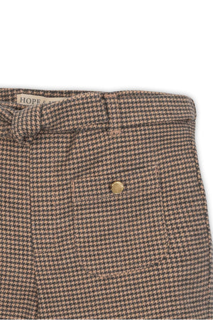Close-up of camel houndstooth wide-leg pants featuring a faux waist tie and a gold button detail. Made from organic cotton.