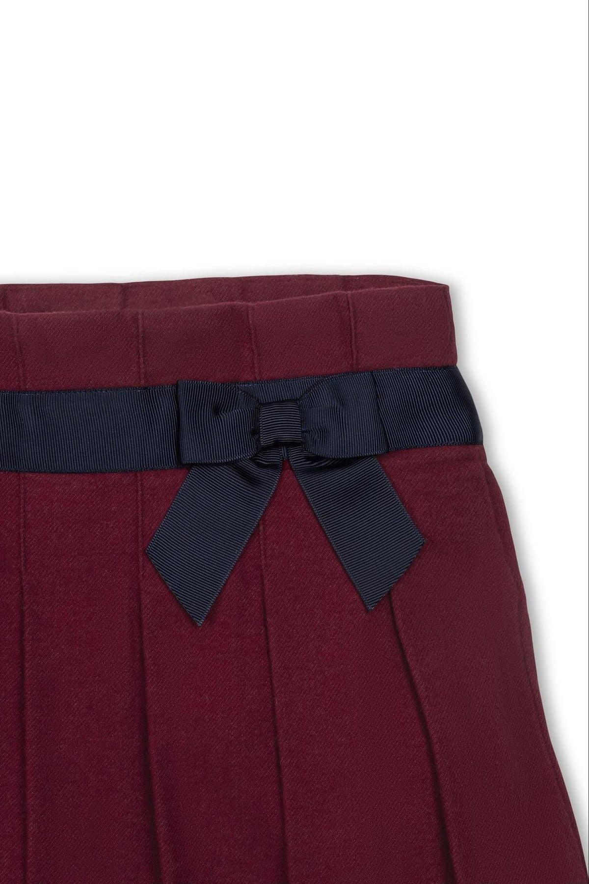 Close-up of a dark red pleated skirt featuring a navy blue bow detail at the waist, made from organic cotton.