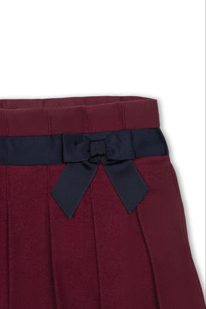 Close-up of a dark red pleated skirt featuring a navy blue bow detail at the waist, made from organic cotton.