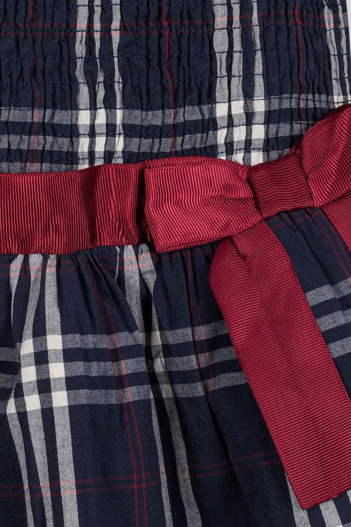 Close-up of a navy plaid dress featuring a smocked bodice and a maroon ribbon belt, showcasing organic cotton material.