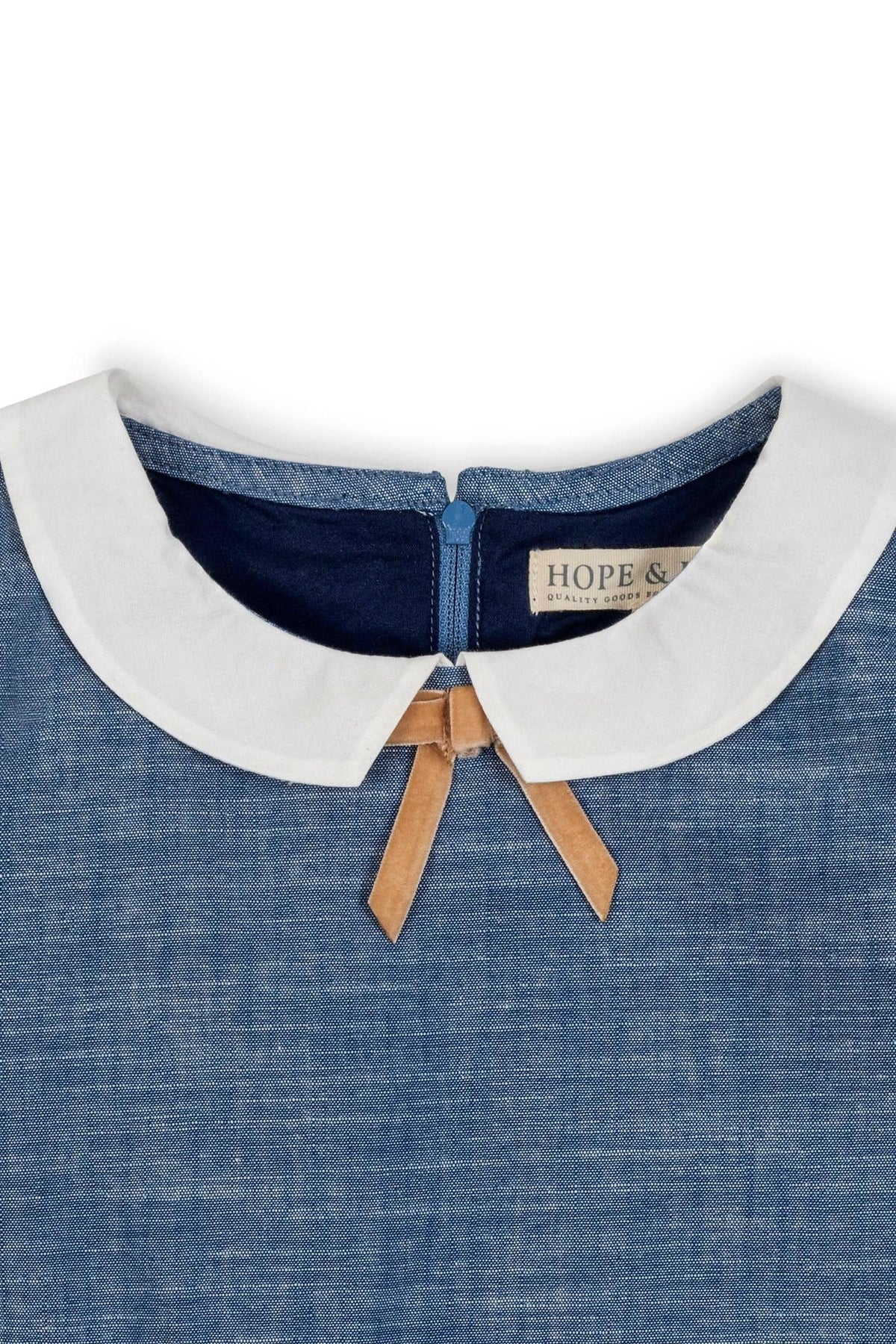 Close-up of a chambray dress collar featuring a white Peter Pan collar with a bow detail. The dress is made from organic cotton, showcasing sustainable fashion for toddlers and kids.