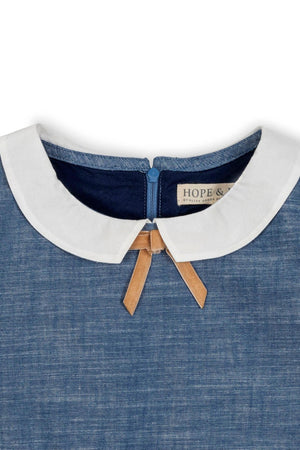 Close-up of a chambray dress collar featuring a white Peter Pan collar with a bow detail. The dress is made from organic cotton, showcasing sustainable fashion for toddlers and kids.