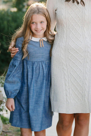 A girl wearing a chambray organic cotton dress with a Peter Pan collar stands beside a woman.