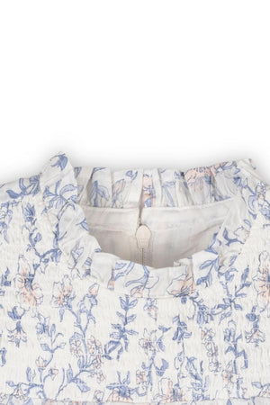 Close-up of a white dress featuring a gray and pink floral print, with a smocked yoke and ruffled neckline.