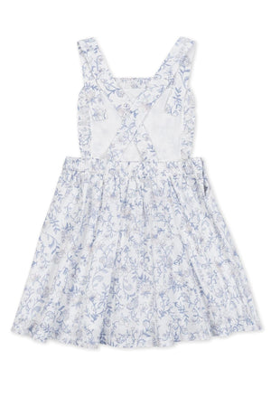 A charming white apron dress featuring a delicate blue floral pattern, ruffle details, and crossback straps. Made from organic cotton, its perfect for toddlers and kids, ensuring comfort and style.