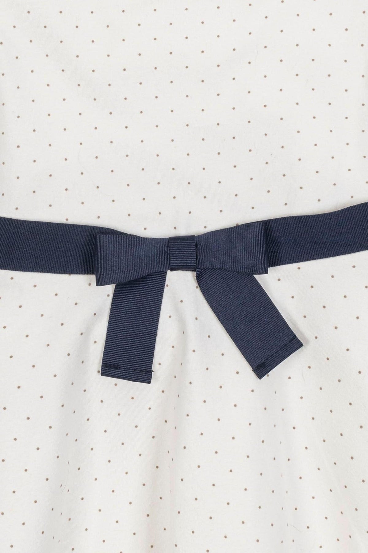 White dress with small pindot pattern and a navy blue ribbon bow at the waist, made from organic cotton.