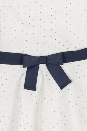 White dress with small pindot pattern and a navy blue ribbon bow at the waist, made from organic cotton.
