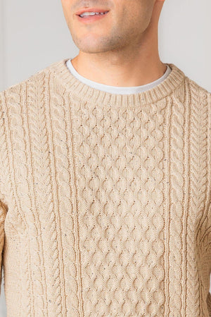 A close-up of a man wearing a natural fleck organic cotton fisherman sweater, featuring a textured allover cable design and classic crewneck style. The sweater showcases a warm, neutral color.
