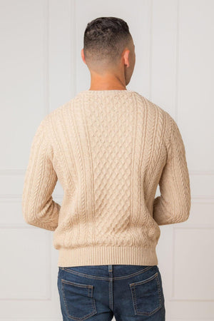 A man is seen from the back, wearing a natural fleck organic cotton fisherman sweater. The cable-knit design adds texture, while the neutral color complements casual denim jeans.