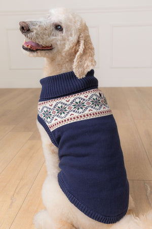 A dog wearing a navy Fair Isle-patterned sweater sits on a wooden floor, showcasing its cozy knit design.