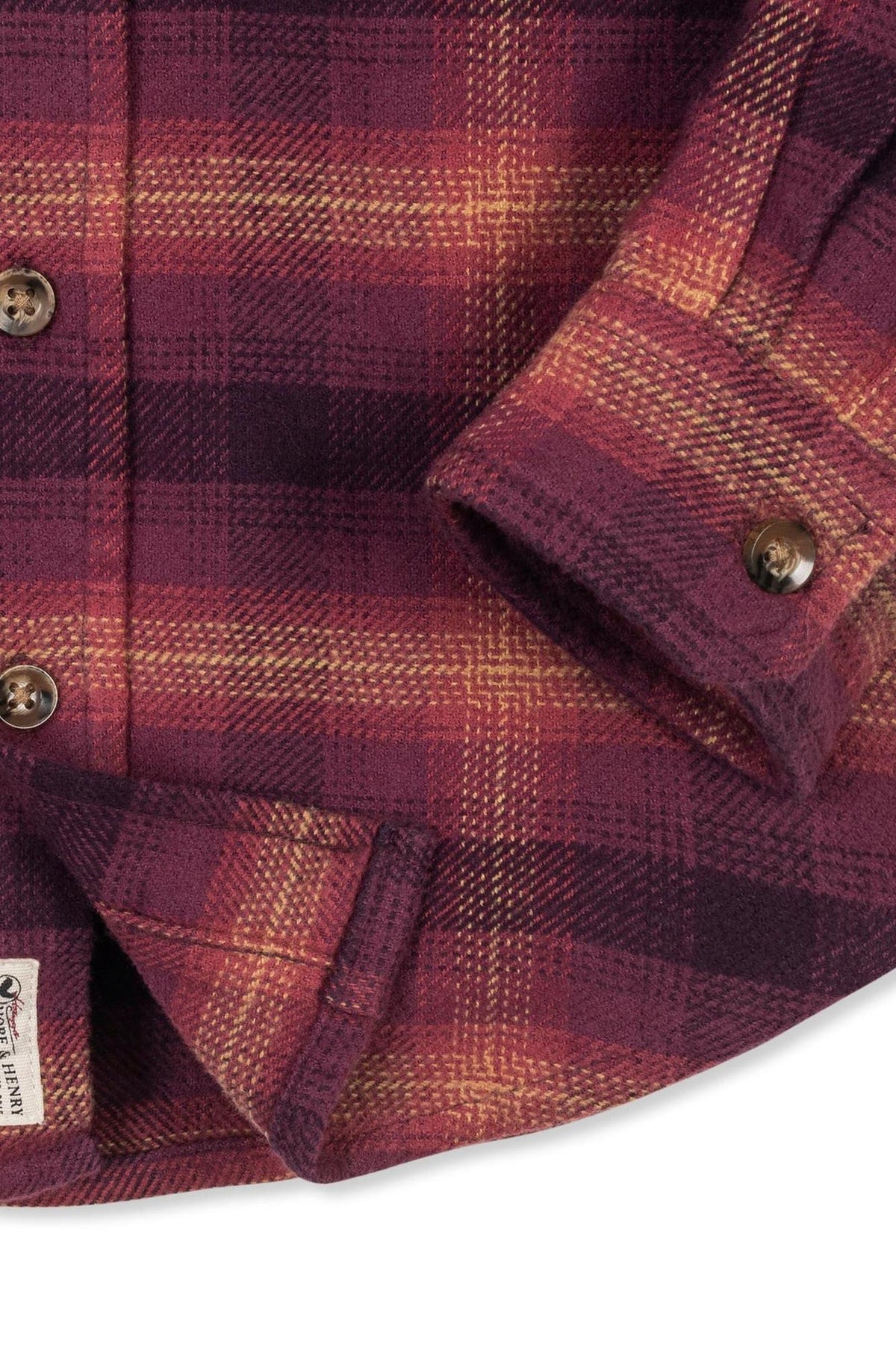 Close-up of a soft plum plaid flannel shirt featuring a buttoned cuff and a label, made from organic cotton.