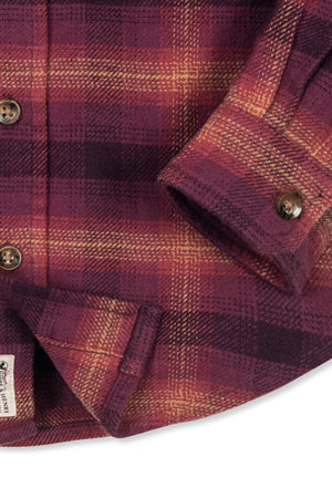 Close-up of a soft plum plaid flannel shirt featuring a buttoned cuff and a label, made from organic cotton.