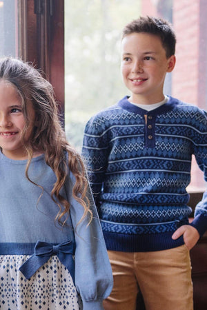 A girl in a light blue sweater smiles beside a boy wearing a navy Fair Isle patterned sweater.