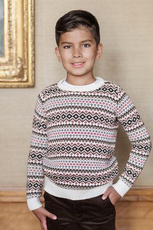 A young boy stands smiling in a cozy, patterned sweater featuring a Fair Isle design in red, black, and cream. The sweater has a crew neck and ribbed cuffs.