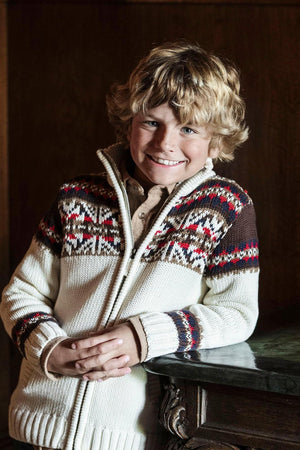 A smiling boy with curly blonde hair wears an ivory sweater featuring a Fair Isle pattern and a full zip.