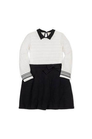 A white and black sweater dress featuring a Peter Pan collar, textured bodice, and a bow at the waist. Made from soft organic cotton, suitable for toddlers and kids.