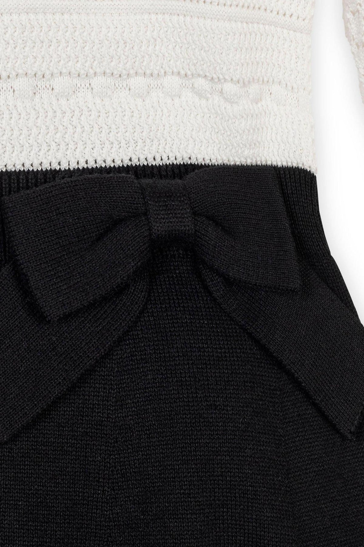 Close-up of a toddler sweater dress featuring a textured white bodice and a black skirt, accented with a stylish bow at the waist, crafted from soft organic cotton.