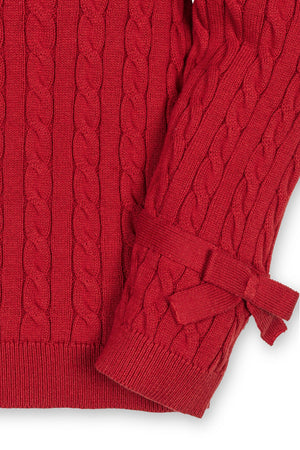 Close-up of a red cable knit sweater featuring puff sleeves and bow details at the cuffs, made from organic cotton.