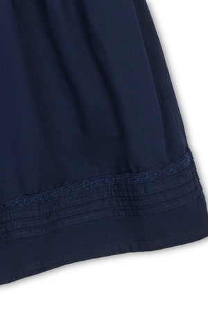 Close-up of a navy dress featuring a pintucked design and delicate embroidered hem, showcasing soft organic cotton material.