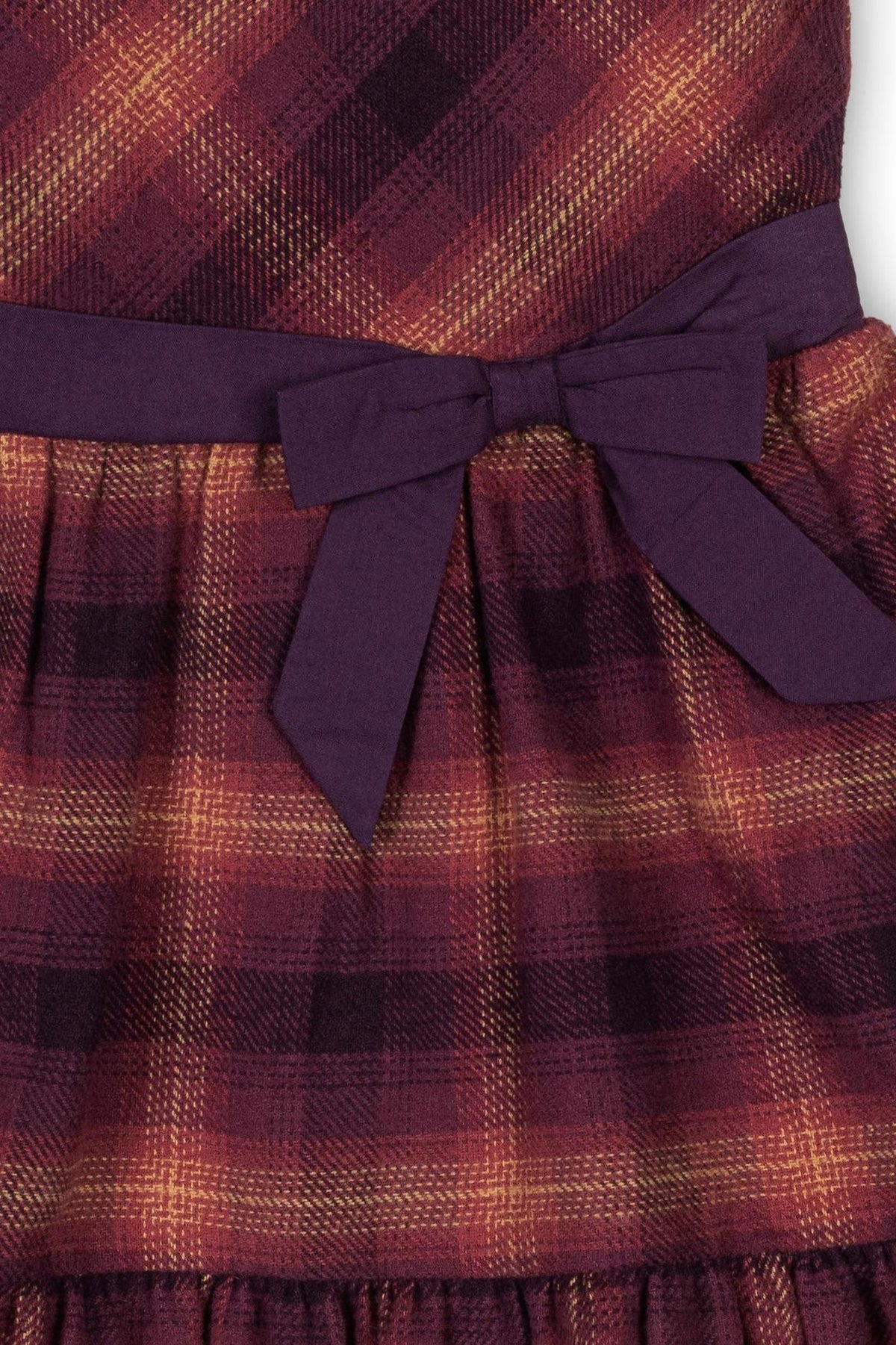 Close-up of a tiered flannel dress in sugar plum plaid, featuring a purple waist tie and soft, organic cotton fabric.