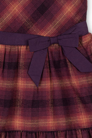 Close-up of a tiered flannel dress in sugar plum plaid, featuring a purple waist tie and soft, organic cotton fabric.