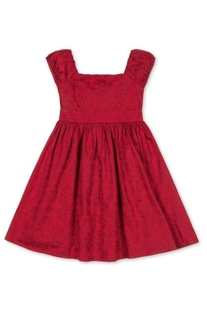 A vibrant fireside red toile dress features delicate puff sleeves and a tailored bodice. Crafted from GOTS certified organic cotton, it offers a soft sheen perfect for special occasions.