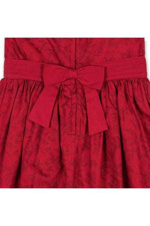 Close-up view of a rich fireside red dress featuring a textured toile pattern, with a tailored bodice and a matching sash tied in a bow at the waist.