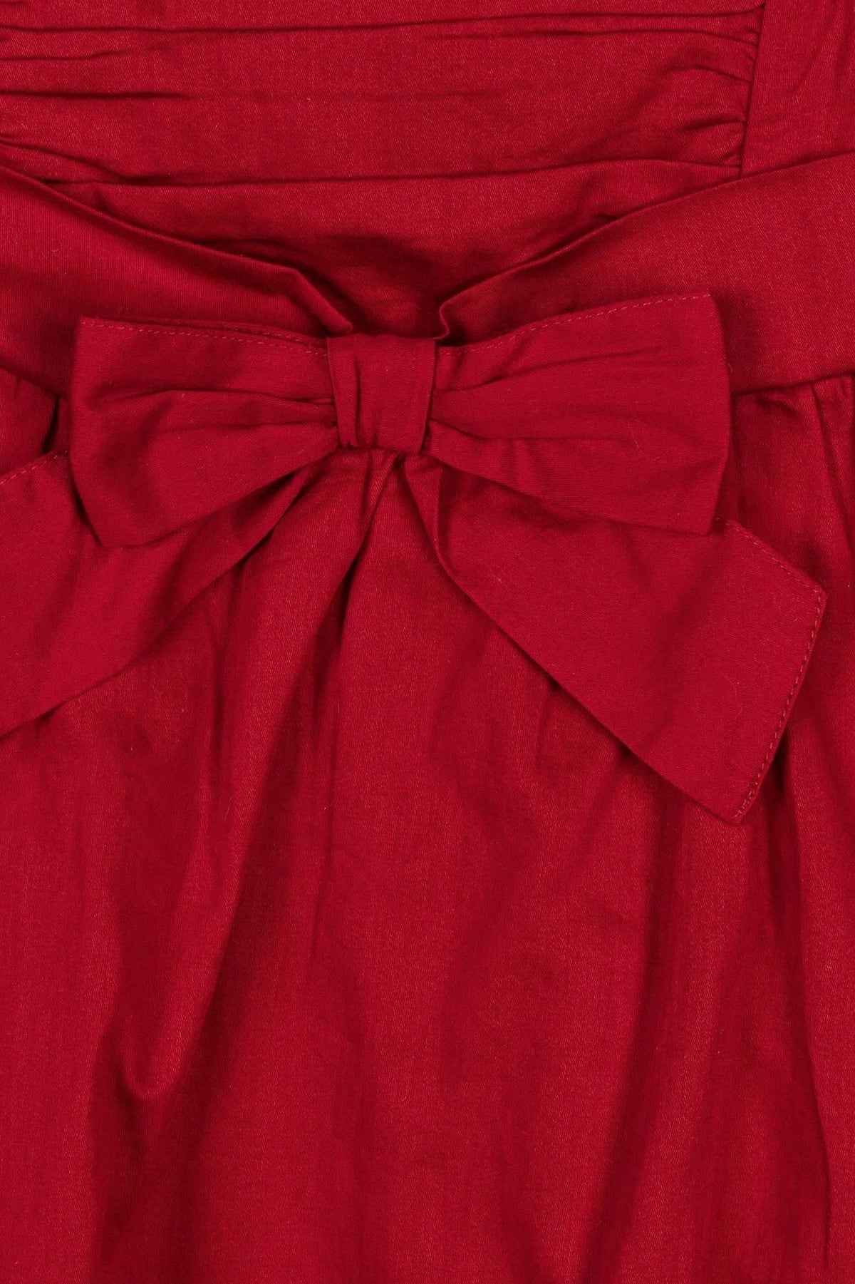 Close-up of a red dress featuring a bow at the waist, made from soft fabric with a ruched bodice.