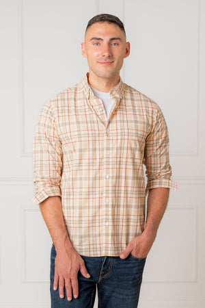 A man stands smiling in a beige and orange plaid long sleeve shirt, made from soft organic cotton. The shirt features a button-down front and is styled with rolled-up sleeves.