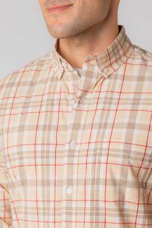 A man models a long-sleeve, button-down shirt featuring a fireside plaid pattern in beige and red. The shirt is made from soft, sustainable organic cotton poplin, emphasizing eco-friendly fashion.