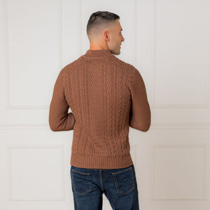 A man is shown from the back wearing a cinnamon heather mock neck cable sweater made of soft organic cotton. The sweater features a textured cable design and ribbed trim.