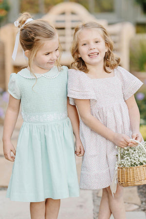 Two young girls in pastel dresses, one mint green with floral embroidery, the other in a floral print.