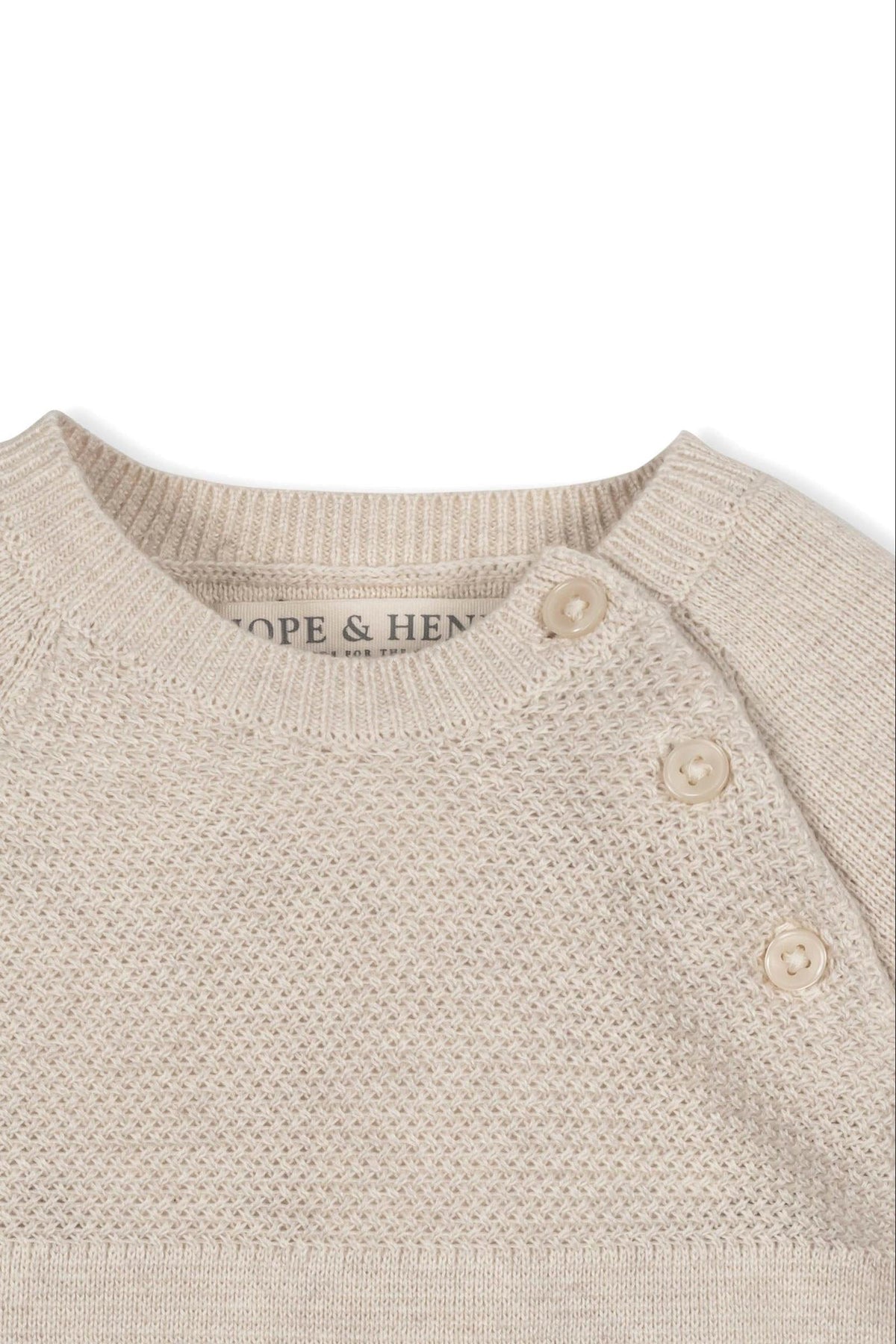 Close-up of a beige, textured sweater romper with button closures, featuring the brand name Hope & Henry on the label.